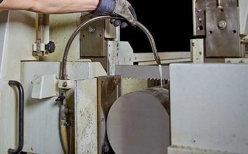 A close-up of a band saw blade cutting through a metal block.